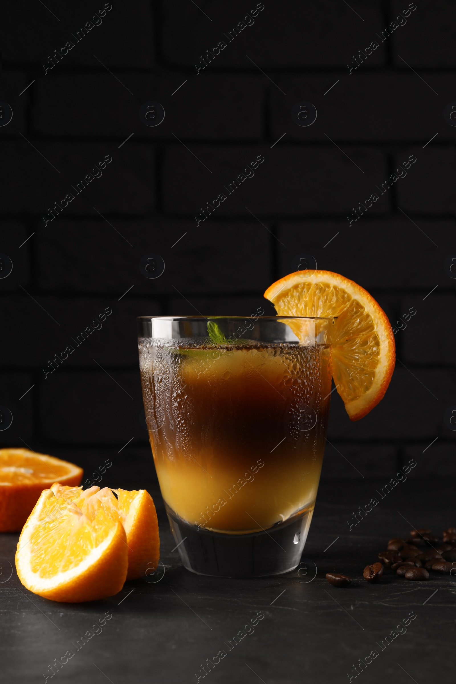 Photo of Tasty refreshing drink with coffee and orange juice on grey table against dark background