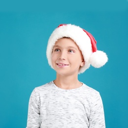 Happy little child in Santa hat on light blue background. Christmas celebration