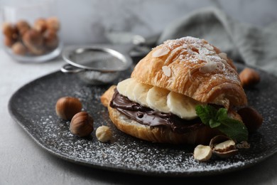 Photo of Delicious croissant with banana, chocolate and hazelnuts on grey table, closeup