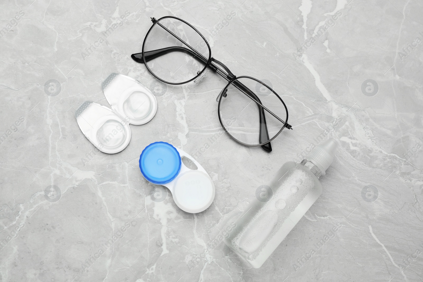 Photo of Packages with contact lenses, case, glasses and drops on light grey marble table, flat lay