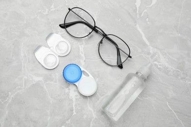 Photo of Packages with contact lenses, case, glasses and drops on light grey marble table, flat lay