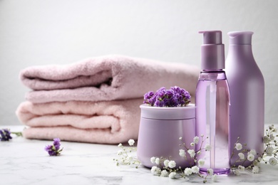 Photo of Set of hair cosmetic products and flowers on white marble table