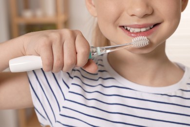 Photo of Little girl brushing her teeth with electric toothbrush in bathroom, closeup