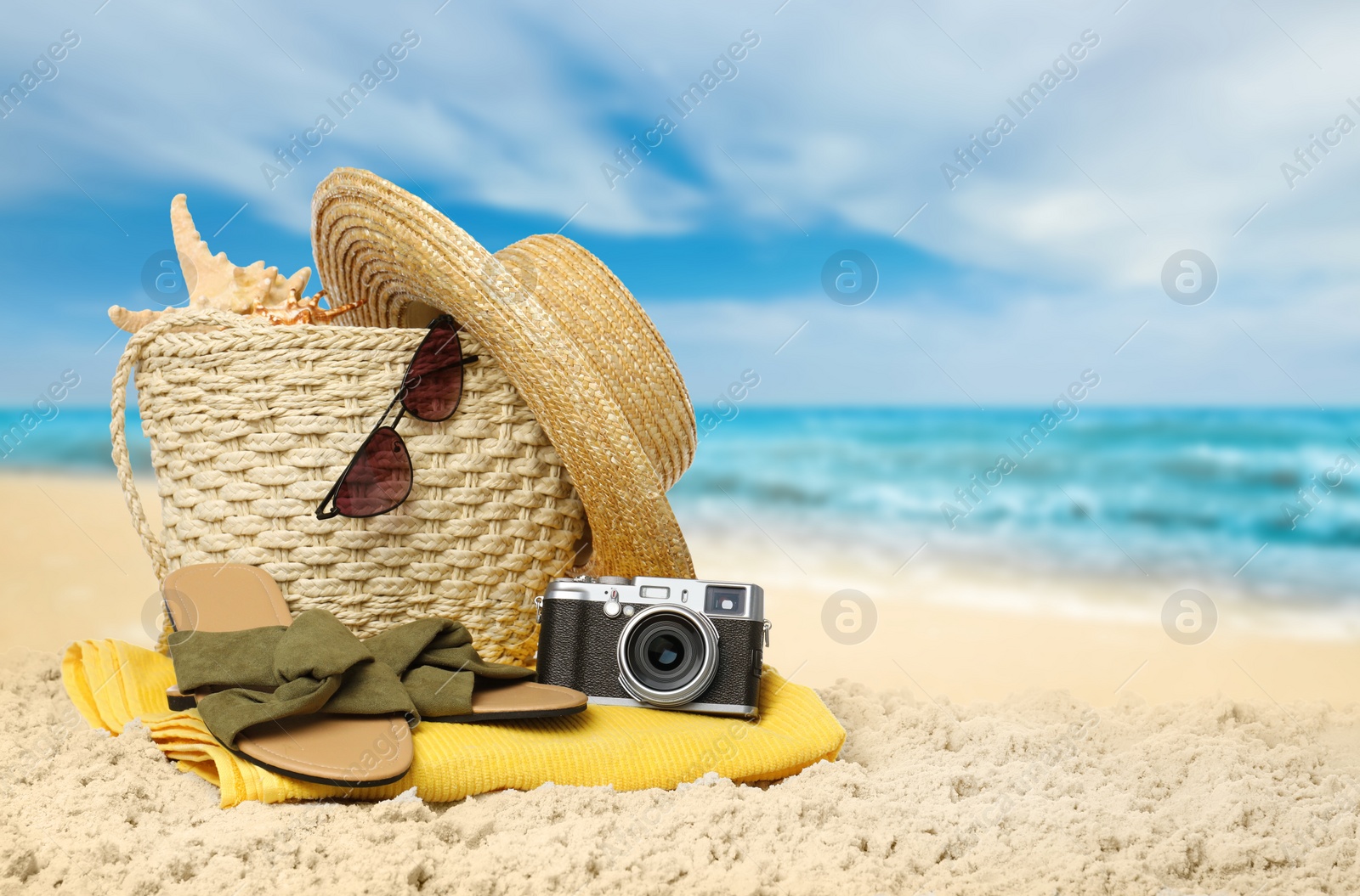 Image of Stylish bag with different accessories on sandy beach near ocean, space for text 