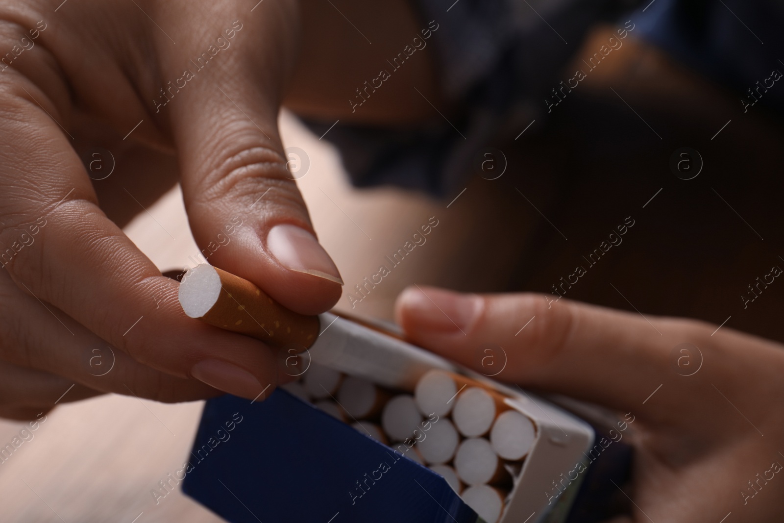 Photo of Woman taking cigarette out of pack at table, closeup