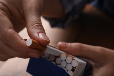 Woman taking cigarette out of pack at table, closeup