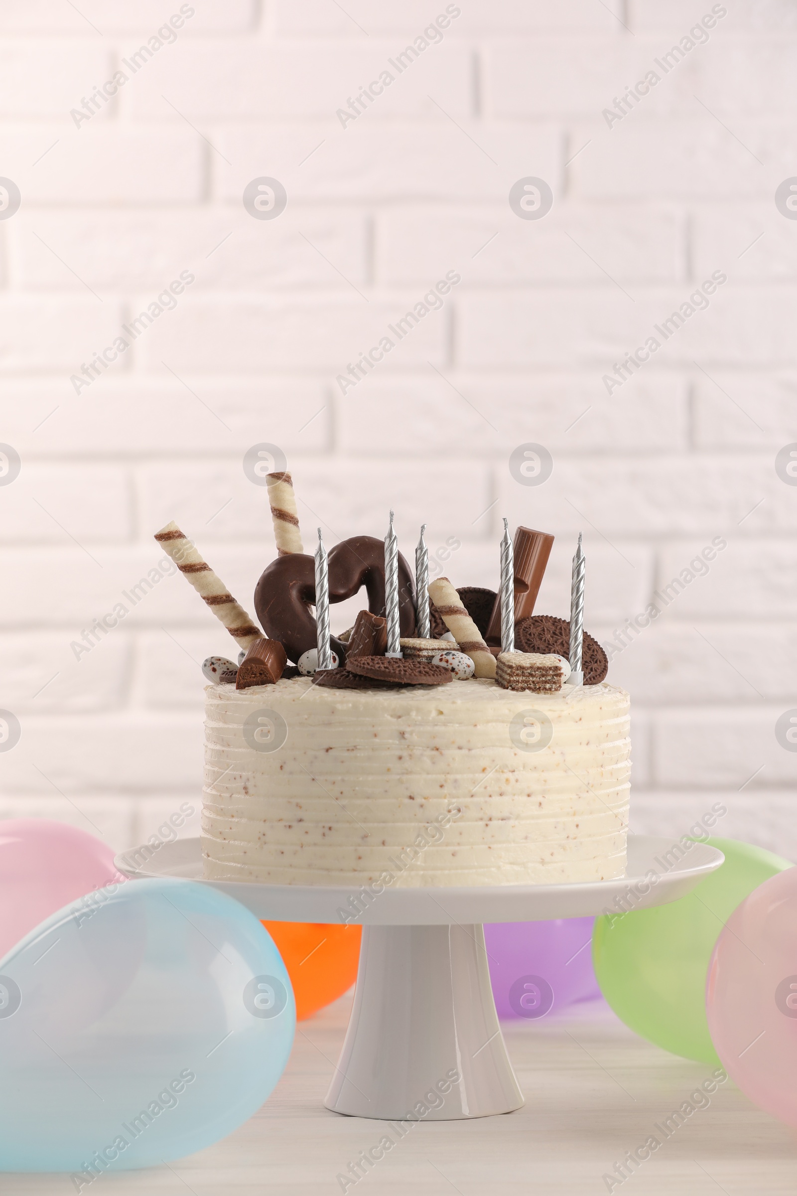 Photo of Delicious cake decorated with sweets and candles among balloons on white table