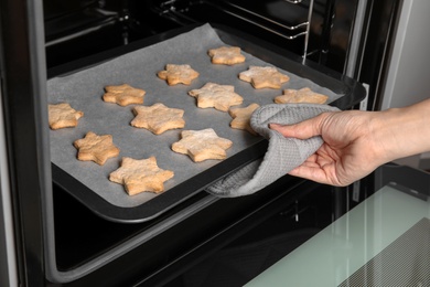 Woman taking baking tray with tasty Christmas cookies out of oven