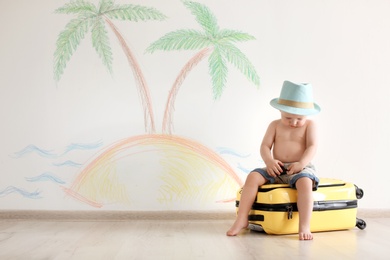 Adorable little child playing traveler with suitcase indoors