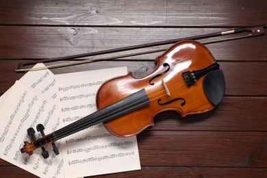 Violin, bow and music sheets on wooden table, top view