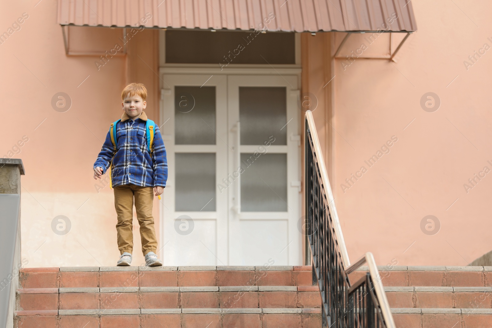 Photo of Cute boy with backpack standing near school