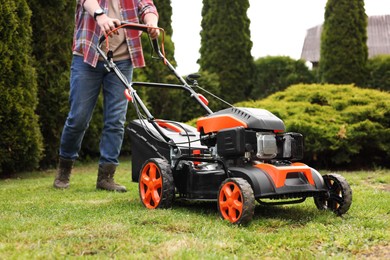 Photo of Man cutting green grass with lawn mower in garden, closeup