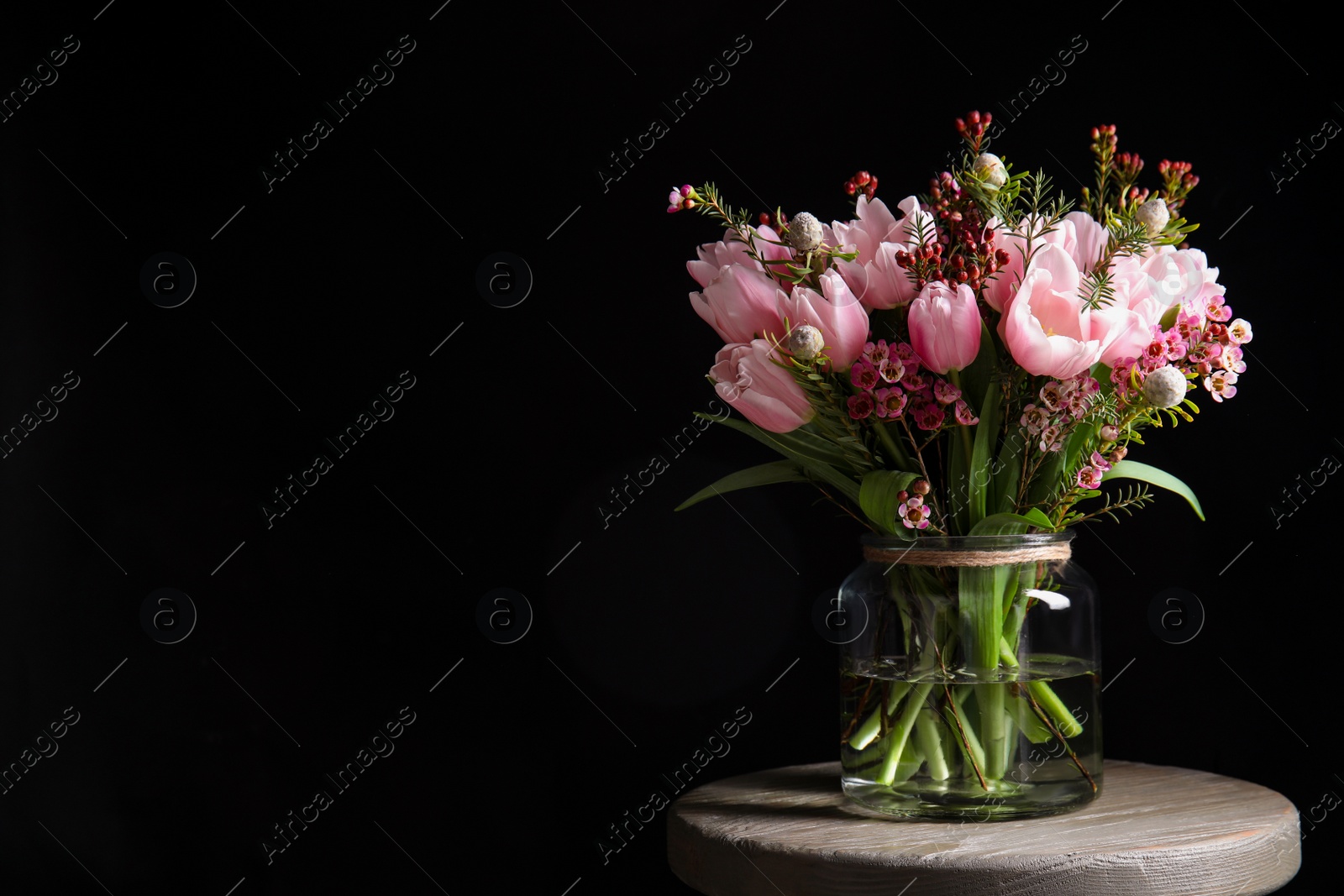 Photo of Beautiful bouquet with spring pink tulips on wooden table against black background. Space for text