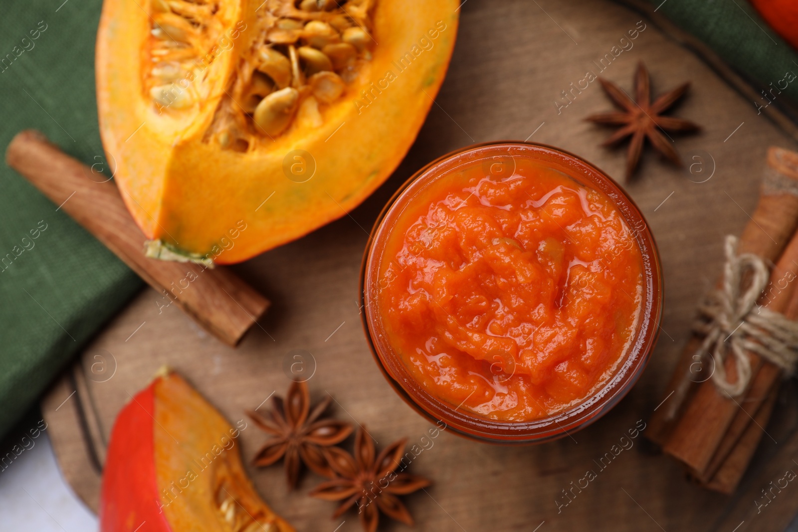 Photo of Jar of delicious pumpkin jam and ingredients on wooden board, flat lay