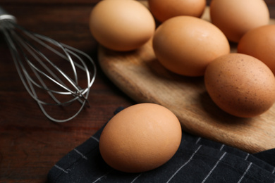 Photo of Chicken eggs and whisk on wooden table, closeup