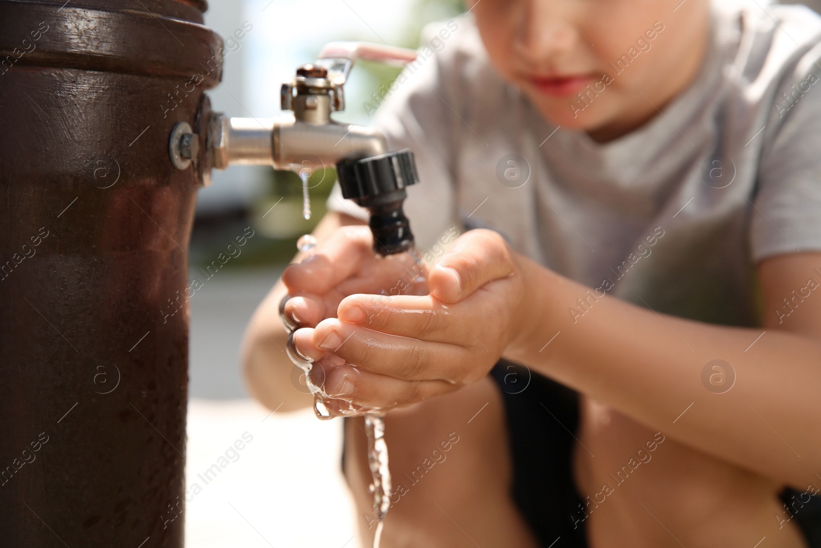 Photo of Water scarcity. Little boy drinking water from tap outdoors, closeup