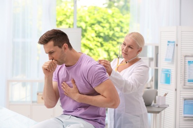 Doctor examining coughing young man at clinic