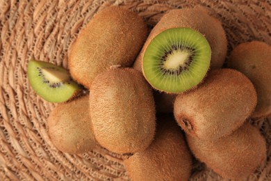 Photo of Heap of whole and cut fresh kiwis on wicker mat, flat lay