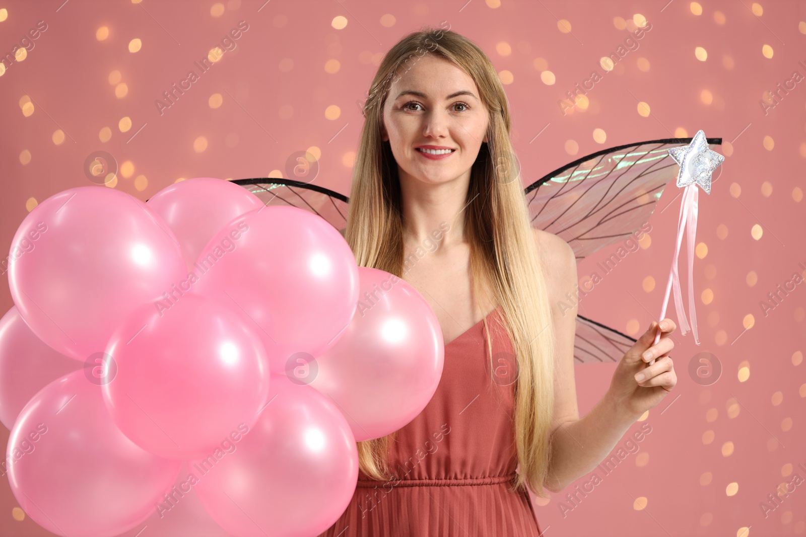 Photo of Beautiful girl in fairy costume with wings, magic wand and balloons on pink background