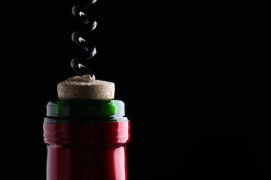 Photo of Opening wine bottle with corkscrew on dark background, closeup. Space for text