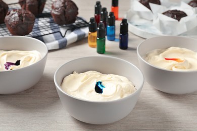 Photo of Bowls of different cream with food coloring on white wooden table