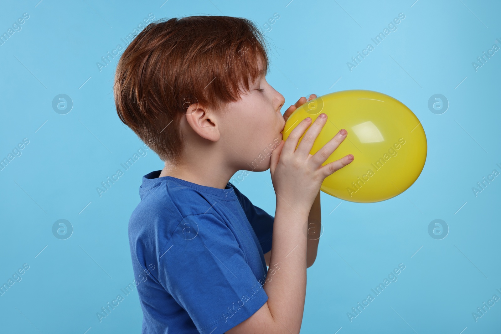 Photo of Boy inflating yellow balloon on light blue background