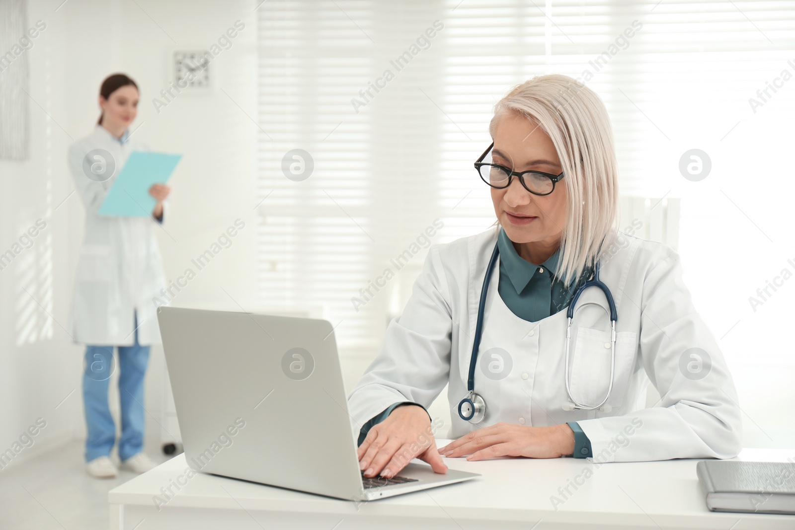 Photo of Mature female doctor working with laptop at table in office