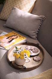 Photo of Tray with flowers in cup and delicious cookies on sofa indoors