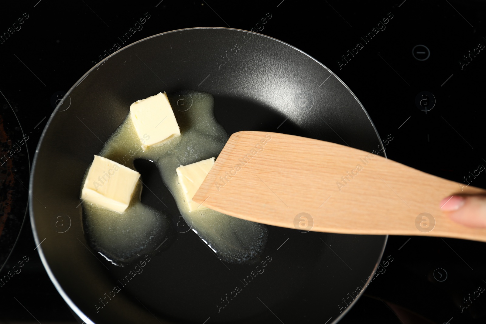 Photo of Woman stirring melting butter in frying pan on cooktop, top view