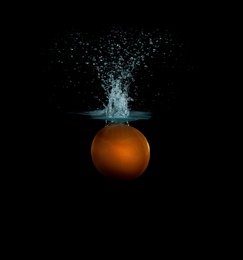 Photo of Grapefruit falling down into clear water against black background