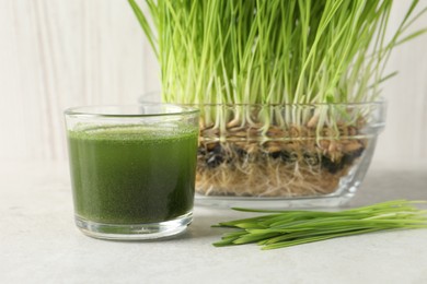Photo of Wheat grass drink in glass and fresh sprouts on light table