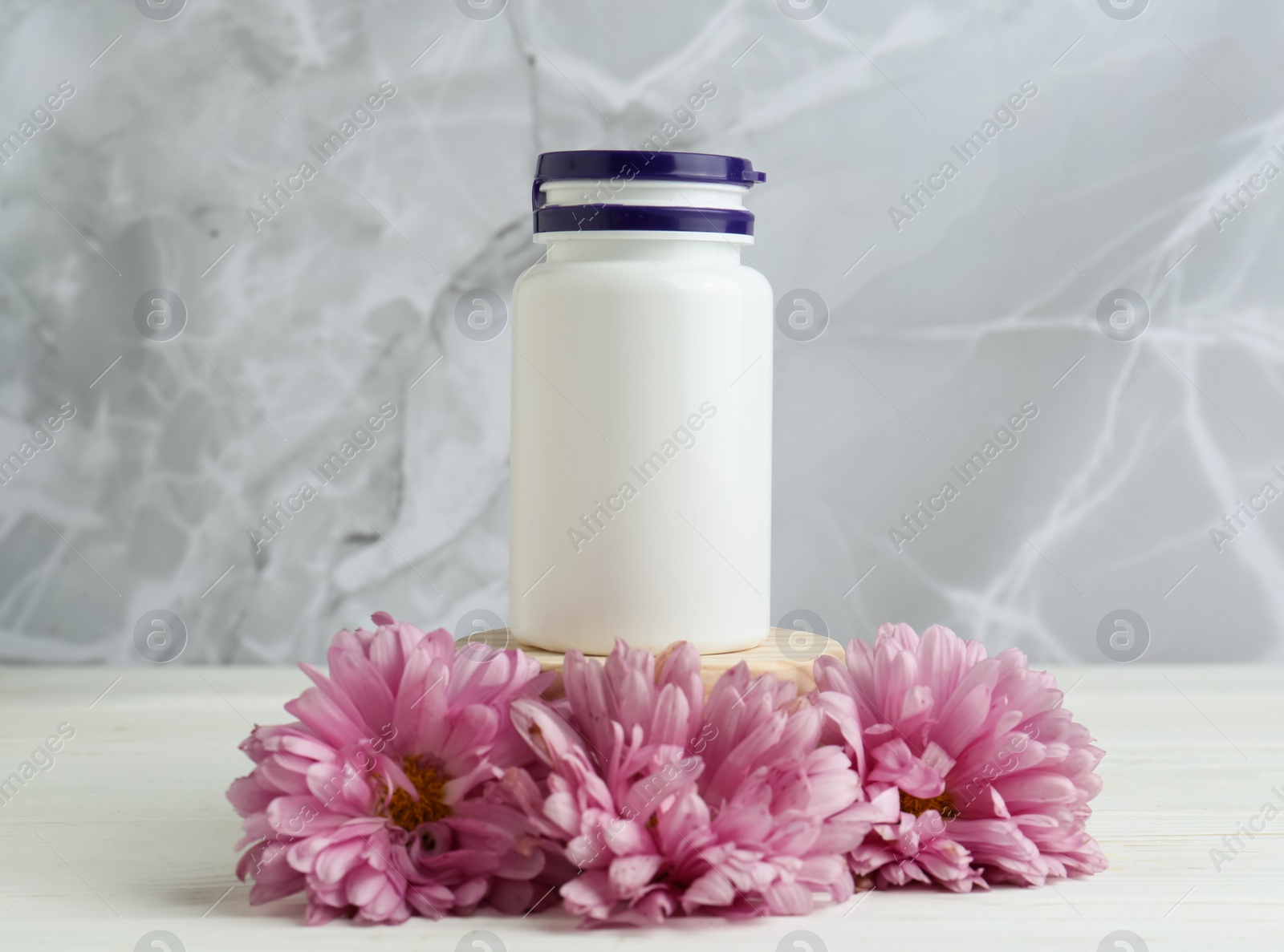 Photo of Medical bottle and pink flowers on white wooden table