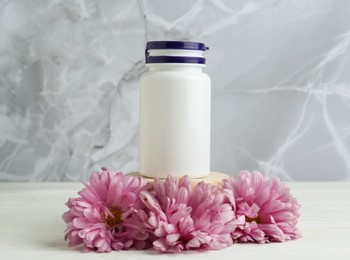 Photo of Medical bottle and pink flowers on white wooden table