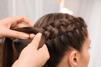 Photo of Professional stylist braiding client's hair in salon, closeup