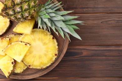 Photo of Pieces of tasty ripe pineapple on wooden table, top view. Space for text