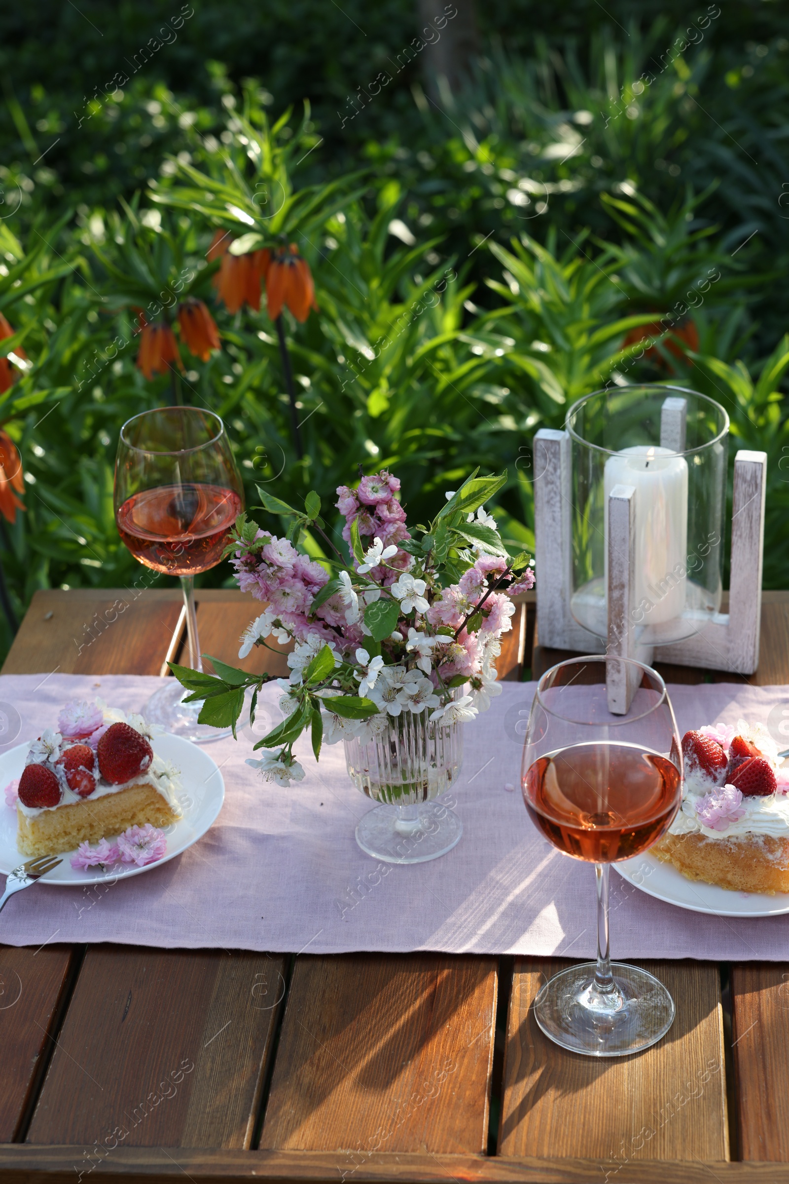 Photo of Vase with spring flowers, wine and cake on table served for romantic date in garden