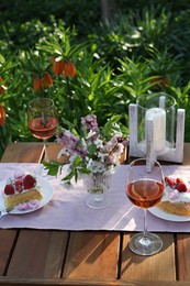 Vase with spring flowers, wine and cake on table served for romantic date in garden