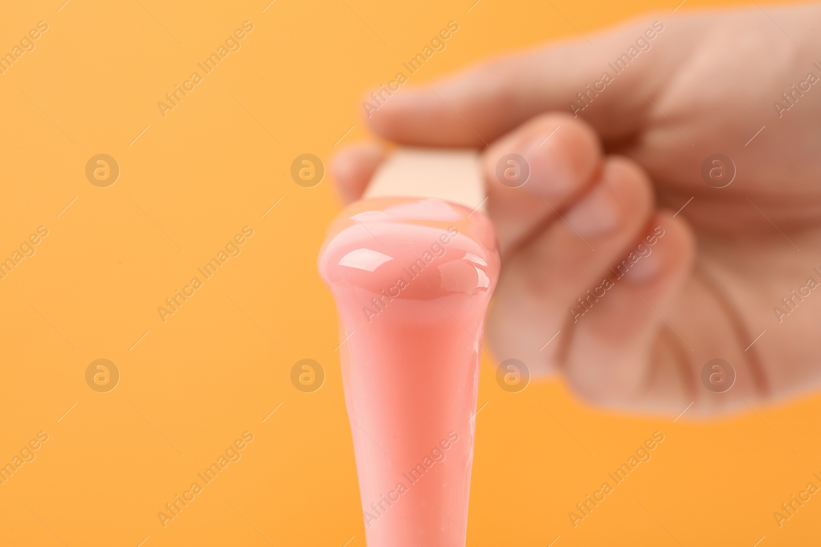 Photo of Woman holding spatula with hot depilatory wax on orange background, closeup