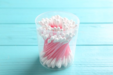 Plastic container with cotton swabs on wooden background