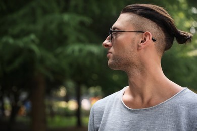 Handsome young man in stylish sunglasses at park, space for text