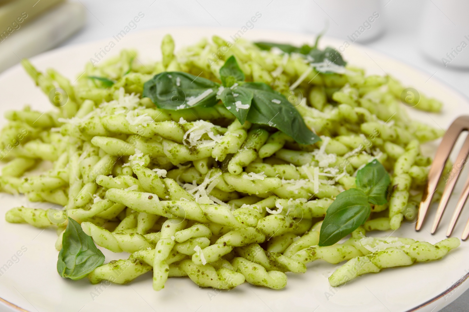 Photo of Plate of delicious trofie pasta with pesto sauce, cheese and basil leaves on table, closeup