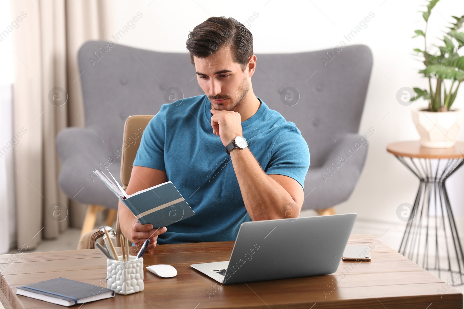 Photo of Handsome young man working with notebook and laptop at table in office
