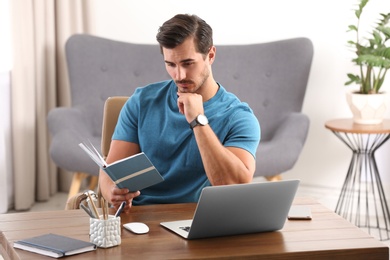 Handsome young man working with notebook and laptop at table in office