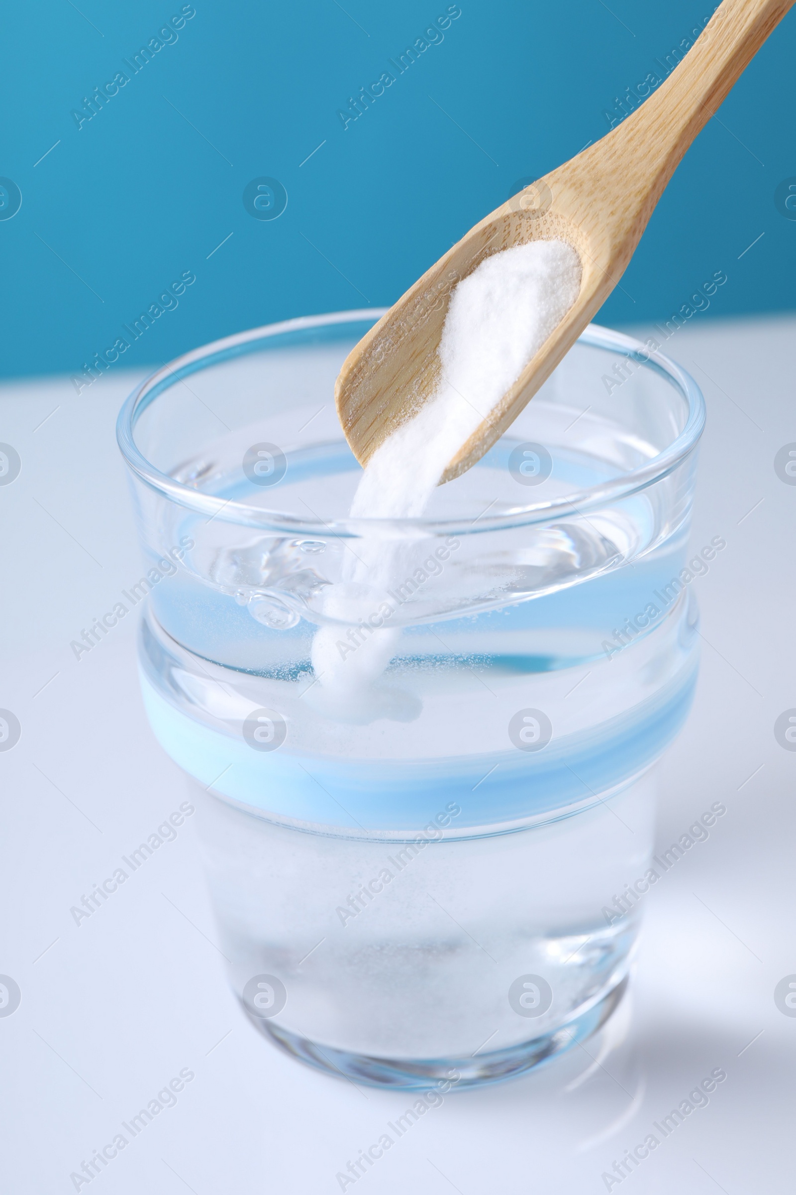 Photo of Adding baking soda into glass of water on color background, closeup