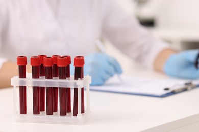 Photo of Doctor with samples of blood in test tubes at white table, selective focus