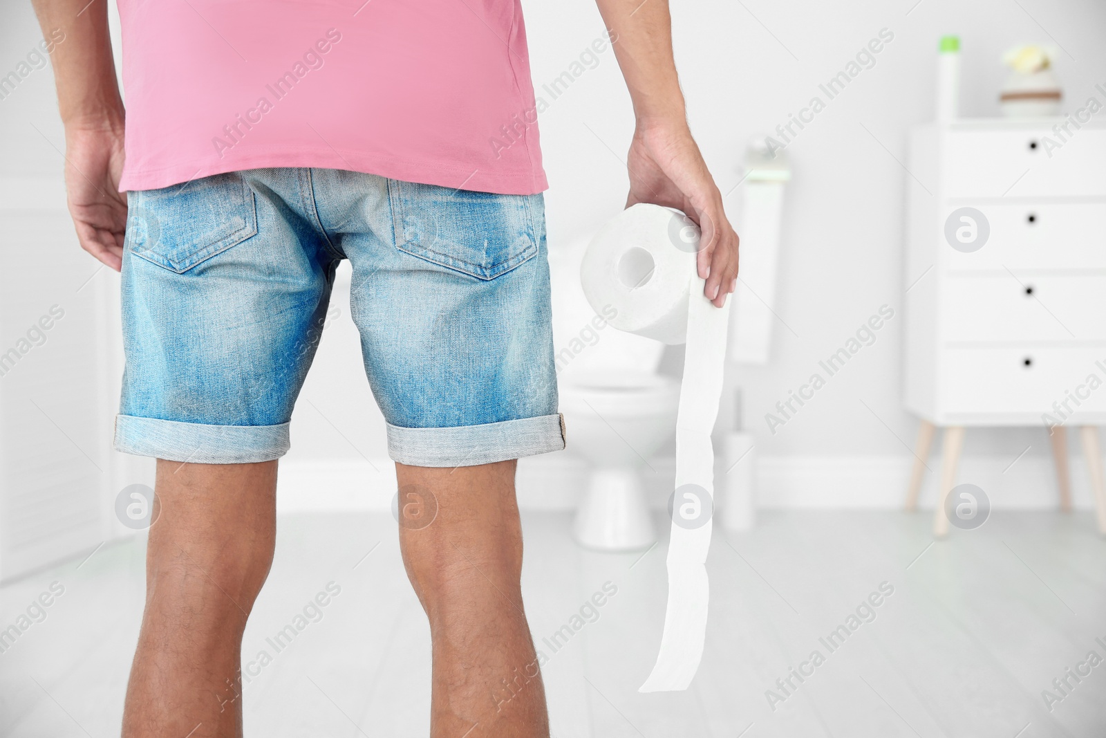 Photo of Young man with bath tissue standing near toilet bowl at home