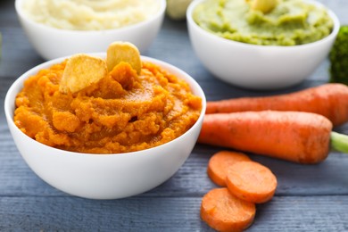 Photo of Bowl with tasty carrot puree and ingredients on light blue wooden table, closeup