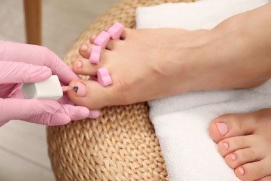 Professional pedicurist painting client`s toenails with polish in beauty salon, closeup