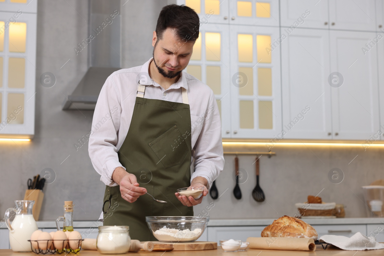 Photo of Making bread. Man putting dry yeast into bowl with flour at wooden table in kitchen