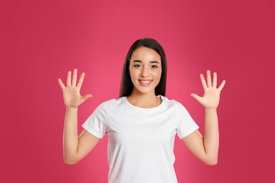Photo of Woman showing number ten with her hands on pink background